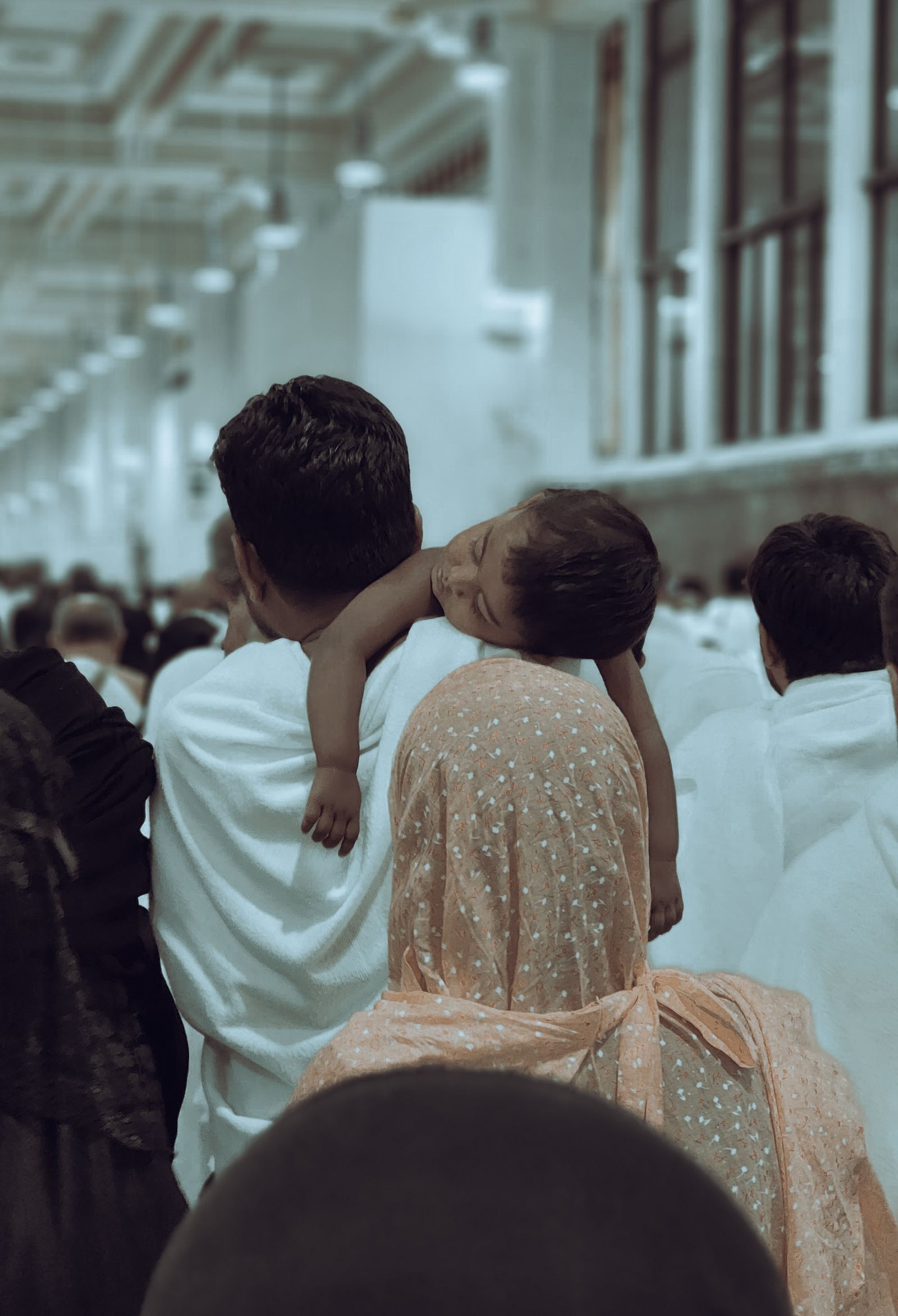 A father in ihram inside the mosque, his child asleep on his shoulder